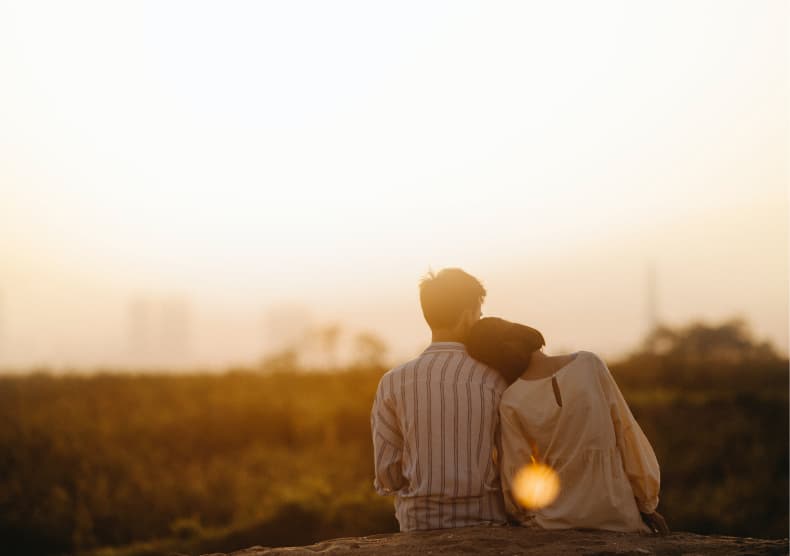 Two people sitting together at golden hour, facing away